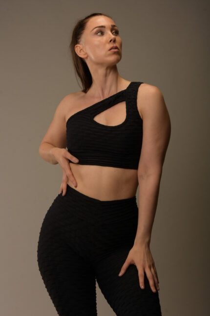 Naisten musta urheilutoppi yhdellä olkaimella ja teksturoidulla kankaalla.